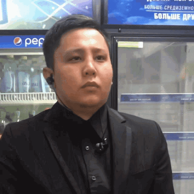 a man in a suit stands in front of a pepsi refrigerator