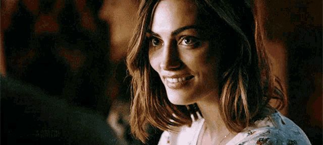 a woman with short hair is smiling and looking at the camera while sitting in front of a man .