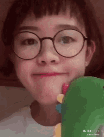 a young girl wearing glasses is holding a stuffed animal in her mouth .
