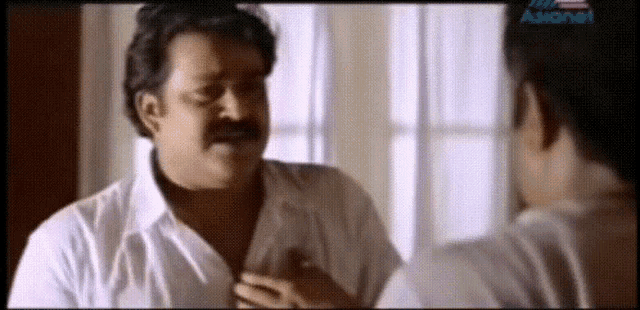 a man in a white shirt is talking to another man with asianet written on the bottom of the screen