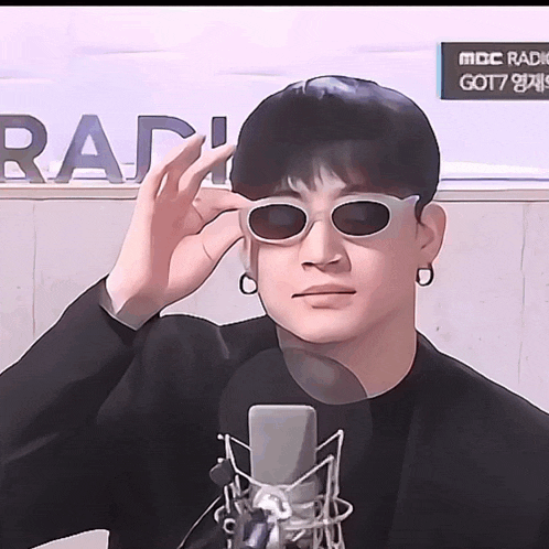 a man wearing sunglasses stands in front of a microphone