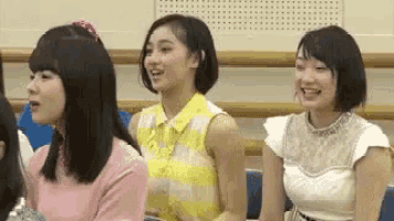 three young women are sitting next to each other in a classroom and smiling .