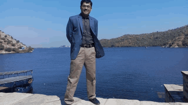 a man in a blue jacket stands in front of a body of water