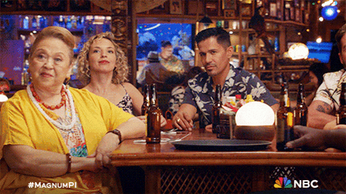 a group of people are sitting at a table with bottles of beer and a nbc logo in the background