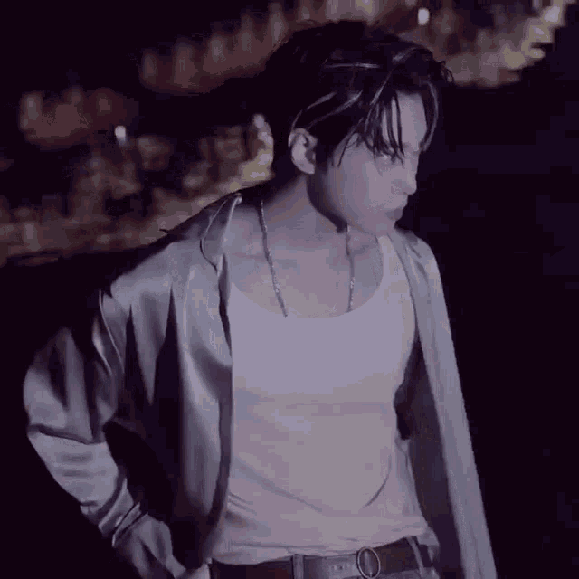 a man wearing a white tank top and a green jacket is standing in the dark