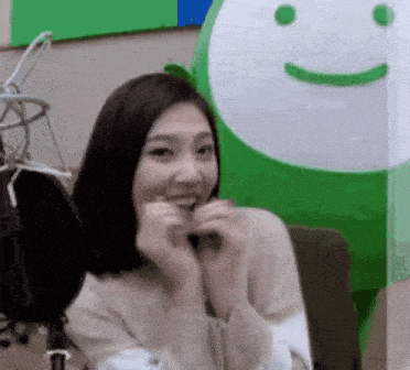 a woman is sitting in front of a green and white balloon with a smiley face on it .
