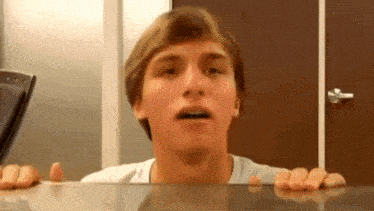 a young man is making a funny face behind a glass table .