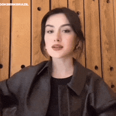 a woman wearing a leather jacket is sitting in front of a wooden wall .