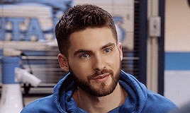a man with a beard wearing a blue hoodie is smiling .