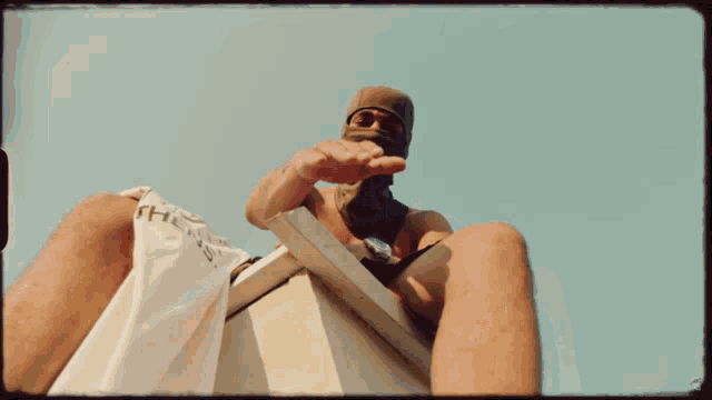 a man wearing a ski mask sits on a ledge with a shirt that says " the " on it
