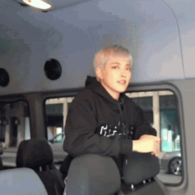 a man wearing a black hoodie with the word hi on it sits in the back seat of a vehicle