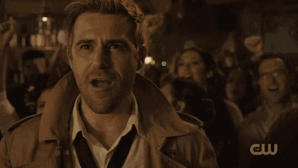 a man in a trench coat stands in front of a crowd with a cw logo on the bottom
