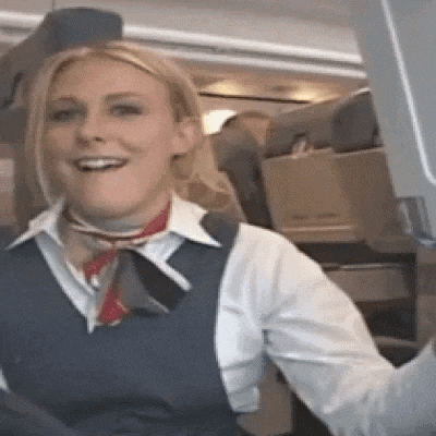 a woman in a blue vest and white shirt is smiling while sitting on an airplane .
