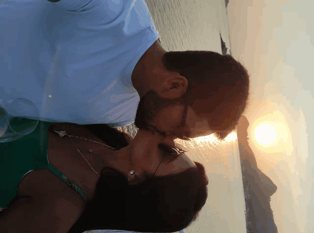 a man and woman kissing in front of the sun