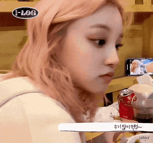 a girl with pink hair is sitting in front of a cell phone and a can of soda .