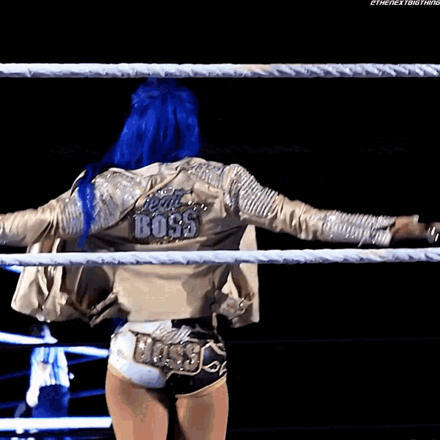 a woman with blue hair is in a wrestling ring wearing a jacket that says boss