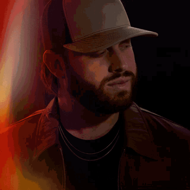 a man with a beard wearing a hat and a jacket with the name jon l. give