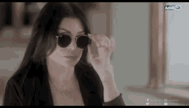 a woman wearing sunglasses and a black jacket is standing in a room .