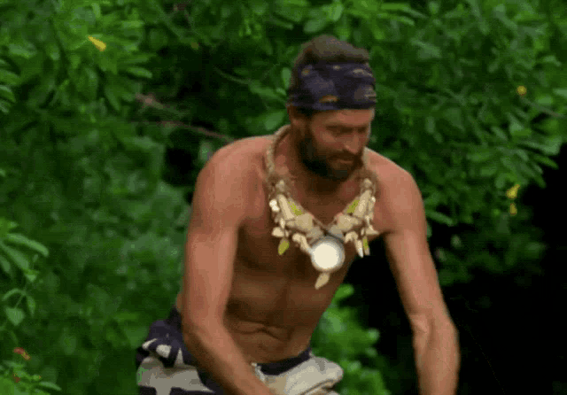 a shirtless man with a necklace around his neck is standing in the jungle .