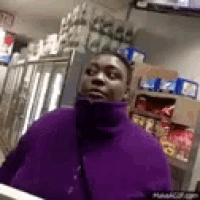 a man in a purple sweater is standing in front of a refrigerator .