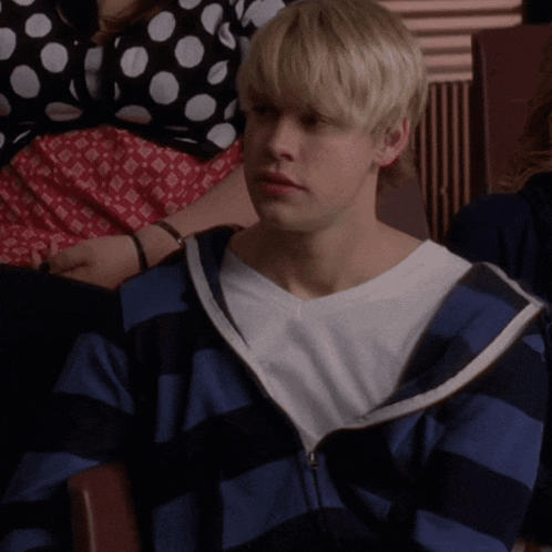 a young man wearing a blue and white striped sweatshirt sits in a chair
