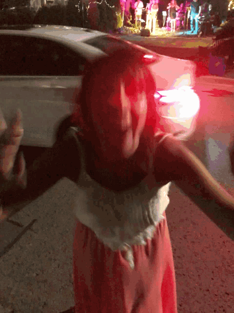 a girl in a pink dress is dancing in front of a white car