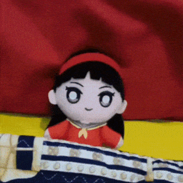 a stuffed doll laying on a bed with a red curtain behind her