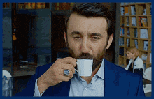 a man in a suit is drinking a cup of coffee .