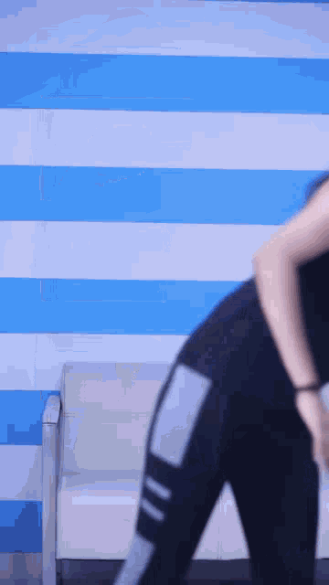a woman is standing in front of a blue and white striped wall and a chair .