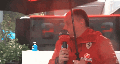 a man in a red ferrari jacket is holding an umbrella and a microphone