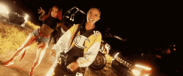 a woman wearing a champion shirt is standing next to a car