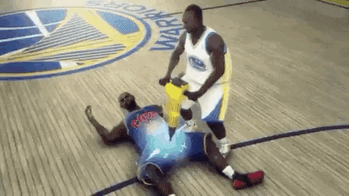 a basketball player is laying on the floor while another player tries to help him up .
