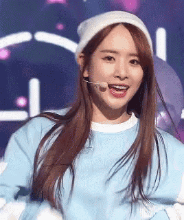 a woman wearing a white hat and a blue sweater is singing into a microphone on a stage .