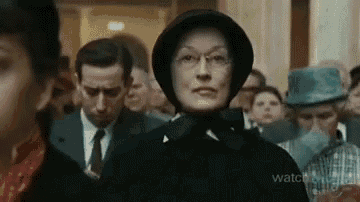 a woman wearing a hat and glasses is standing in a crowd of people .