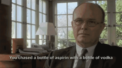 a man in a suit and tie is talking about a bottle of aspirin with a bottle of vodka