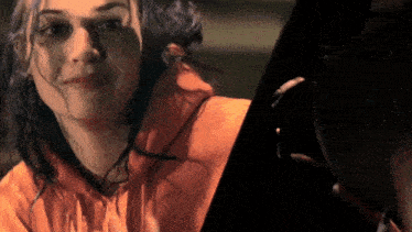 a woman in an orange hoodie is looking at a man in a car