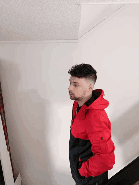 a man in a red and black jacket stands in a corner
