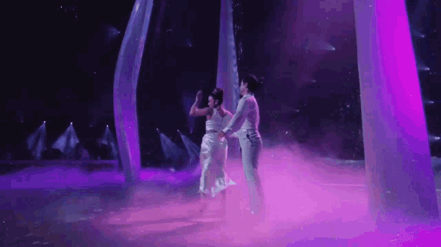 a man and woman are dancing on a stage with purple lights behind them