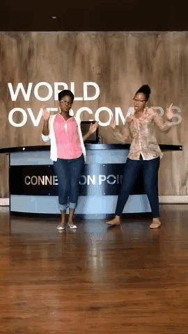 two women dance in front of a sign that says world overcomers