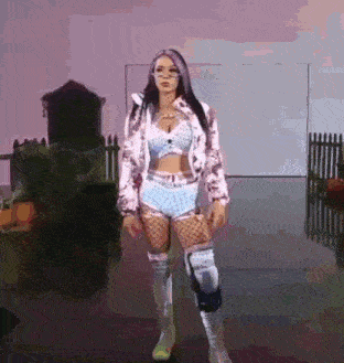 a woman in a pink jacket and blue shorts is standing in a room with pumpkins in the background .