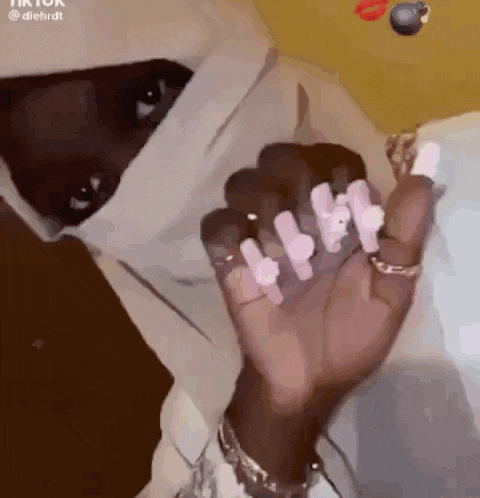 a woman with long nails is wearing a hoodie and holding her hand up .