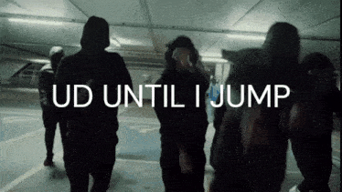 a group of people are walking in a parking garage with the words " ud until i jump " on the screen