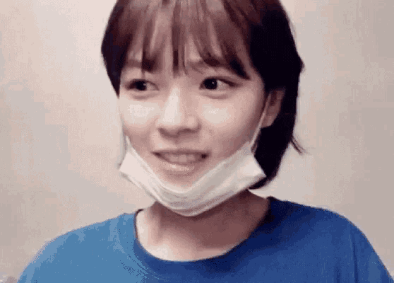a woman wearing a blue shirt and a face mask is making a funny face .