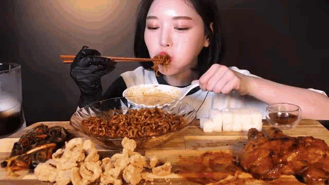 a woman wearing black gloves is eating noodles with chopsticks from a bowl