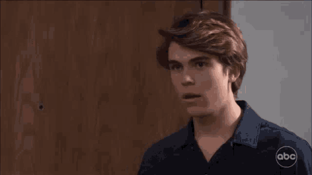 a young man is covering his mouth with his hand in front of a wooden door .