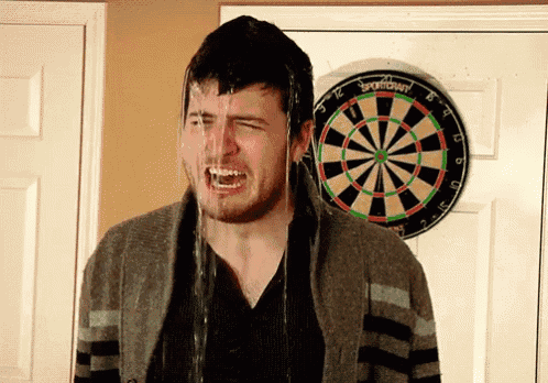 a man is standing in front of a dart board with water pouring out of his face