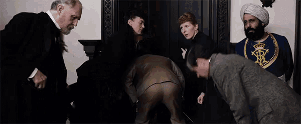 a group of people are standing around a man in a suit and talking to him .