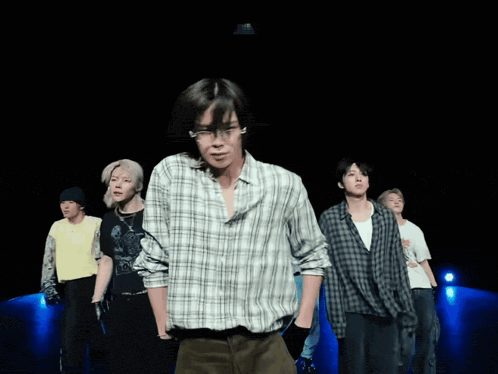 a group of young men are dancing on a stage and one of them is wearing a plaid shirt with the letter m on it