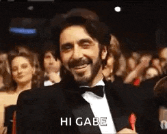 a man in a tuxedo is smiling in front of a crowd and says hi gabe .