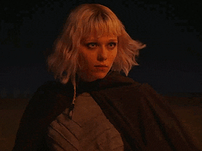 a woman with blonde hair and a cape is standing in the dark .